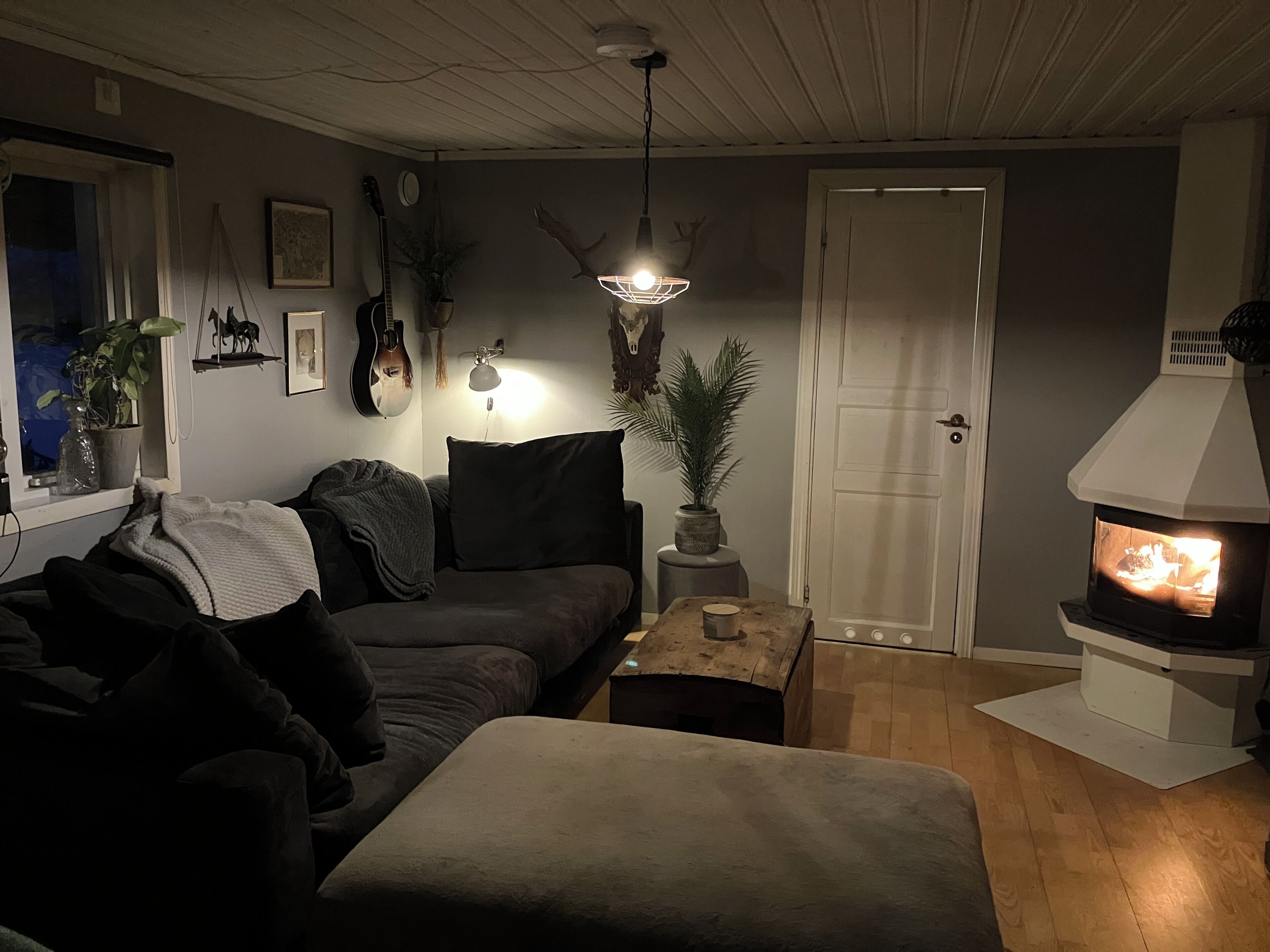 Ett mysigt vardagsrum med en soffa i mörka färger, ett litet träbord, en krukväxt och en öppen spis.