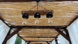 Un espace extérieur abrité, doté d’un plafond en bambou et de rideaux blancs.