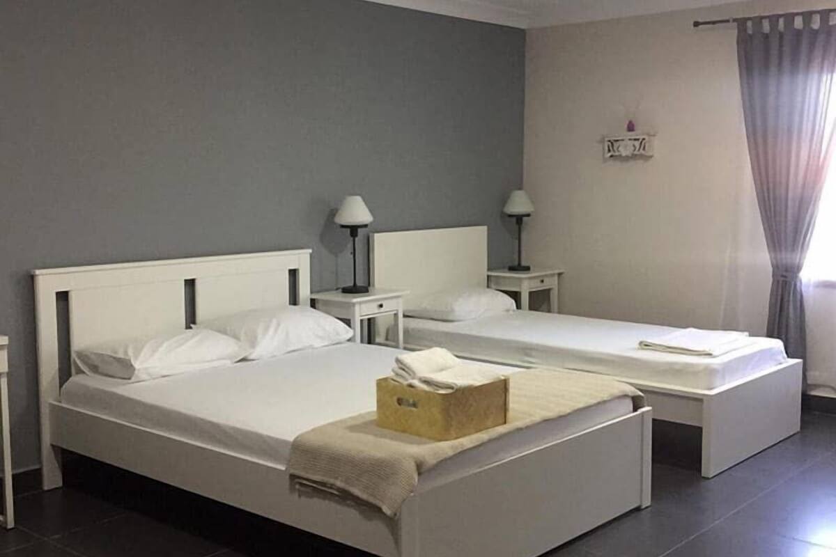 A hotel room with two single beds, a small table with a lamp, a nightstand, and a wall-mounted light fixture.