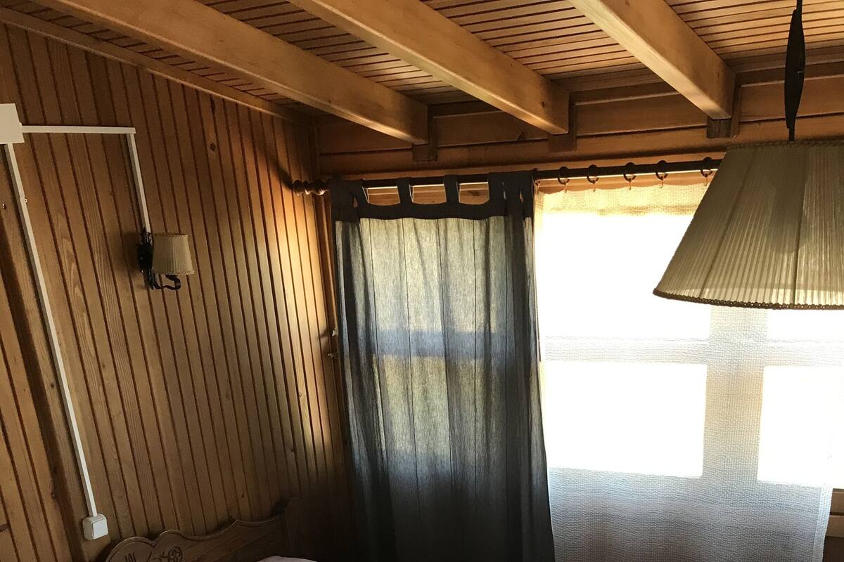 A wooden-paneled room with a bed, a window with curtains, and a lamp.