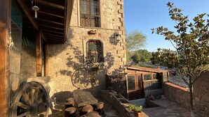 Un bâtiment rustique en pierre, doté d’un porche en bois, de grandes roues et d’un petit arbre.