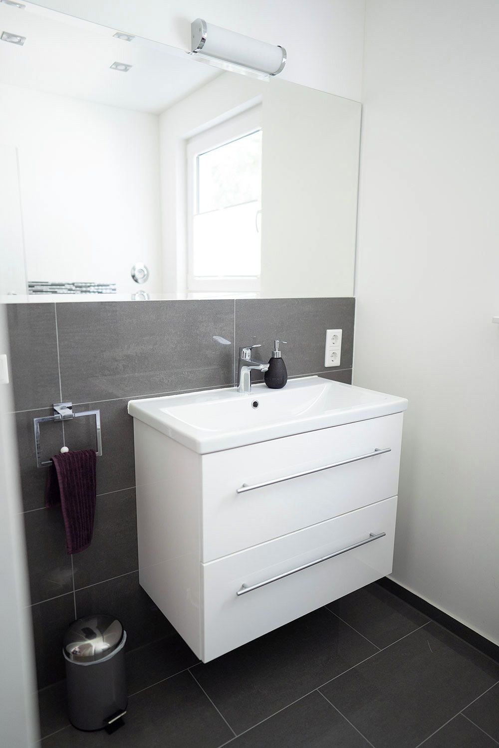 A modern bathroom with a white vanity, a mirror, and a towel rack.