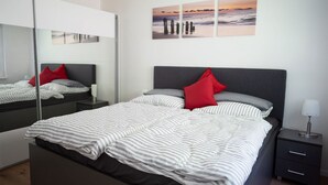 Une chambre moderne avec un grand lit, une table de chevet, une commode, un miroir et un mur orné de trois tableaux.