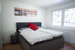 Une chambre moderne avec un grand lit, une table de chevet et une fenêtre donnant sur un paysage verdoyant.