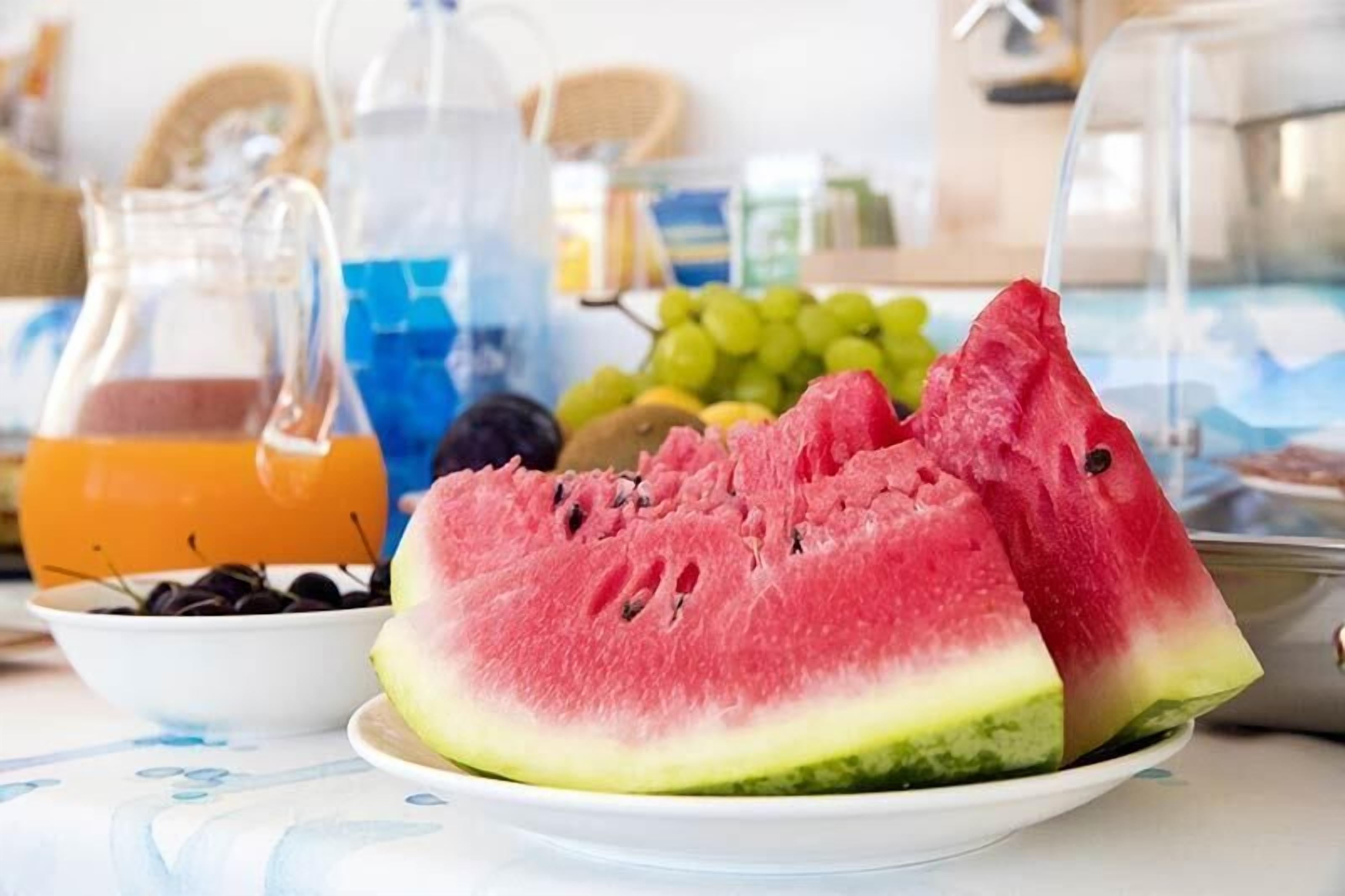 Een tafel met een watermeloen, druiven en een schaal kersen.
