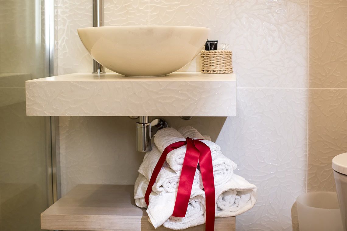 A bathroom with a white sink, a red ribbon-tied towel stack, and a wicker basket.