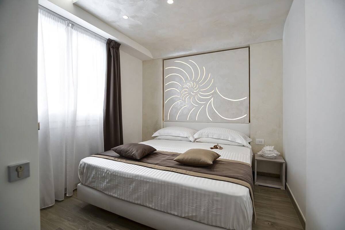Une chambre à coucher moderne avec un grand lit, une tête de lit décorative, une table de chevet et une fenêtre avec des rideaux.