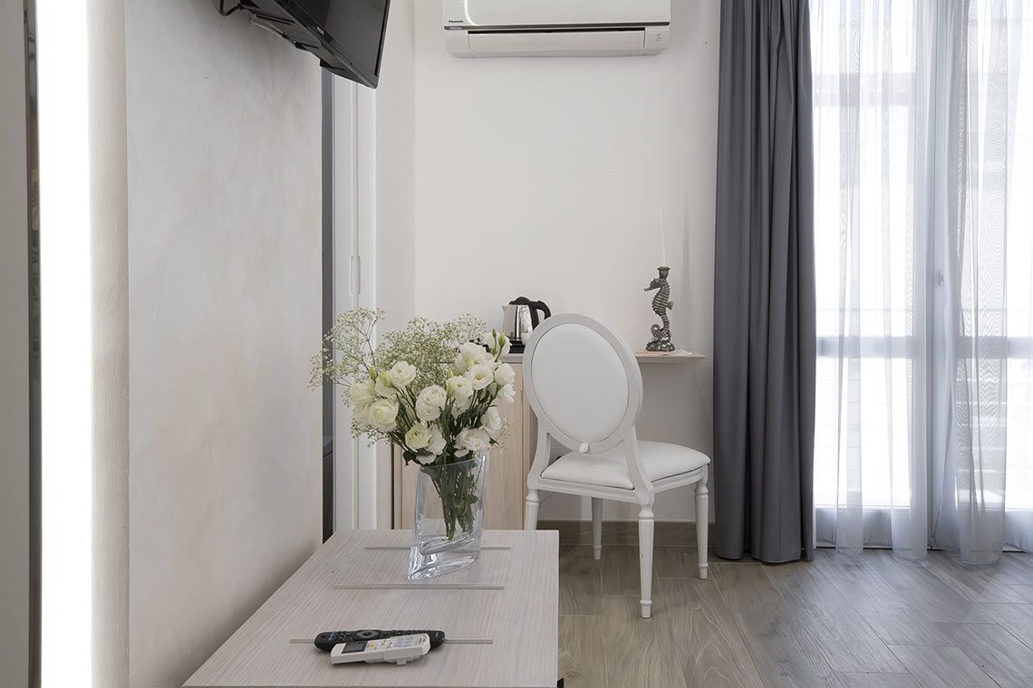 A modern room with a white table, a vase of white flowers, a white chair, and a TV mounted on the wall.