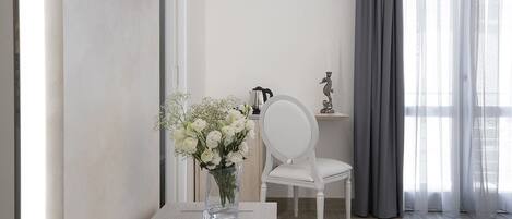 A modern room with a white table, a vase of white flowers, a white chair, and a TV mounted on the wall.