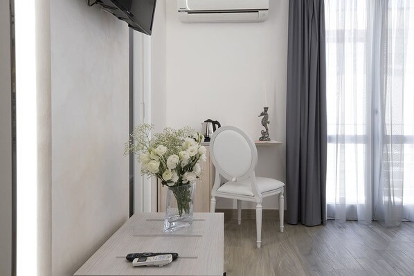 Une pièce moderne avec une table blanche, un vase de fleurs blanches, une chaise blanche et un téléviseur fixé au mur.