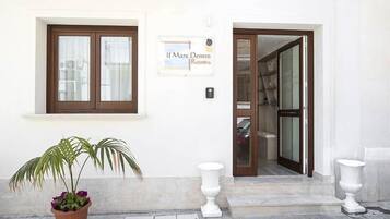 A hotel entrance with a sign reading "Il Mare Dento Rooms," a potted plant, and two white urns.