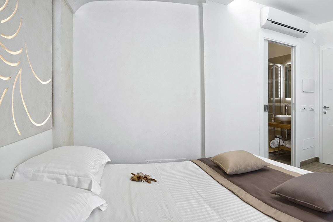 Een moderne slaapkamer met een bed, nachtkastje, spiegel en een badkamer door een open deur zichtbaar.