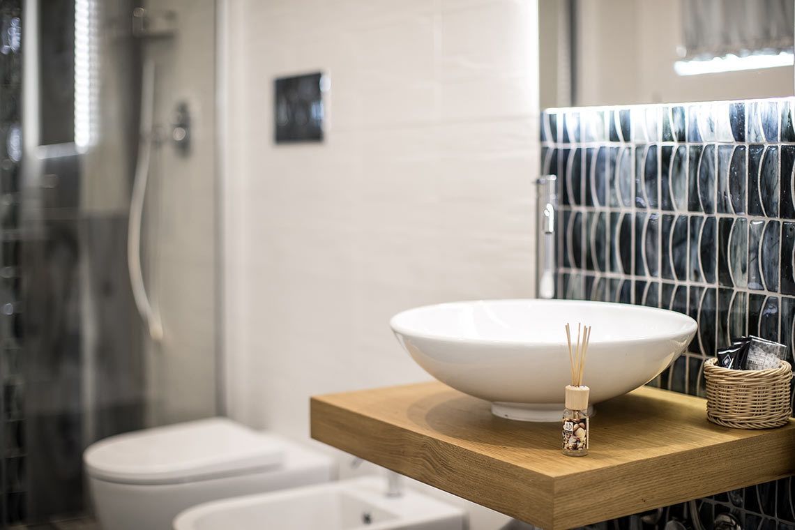 Un baño moderno con un lavamanos blanco grande sobre una encimera de madera, un pequeño difusor de aroma y una cesta de mimbre.