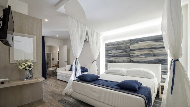 Une chambre à coucher moderne avec un grand lit, une coiffeuse avec un miroir et un téléviseur fixé au mur.