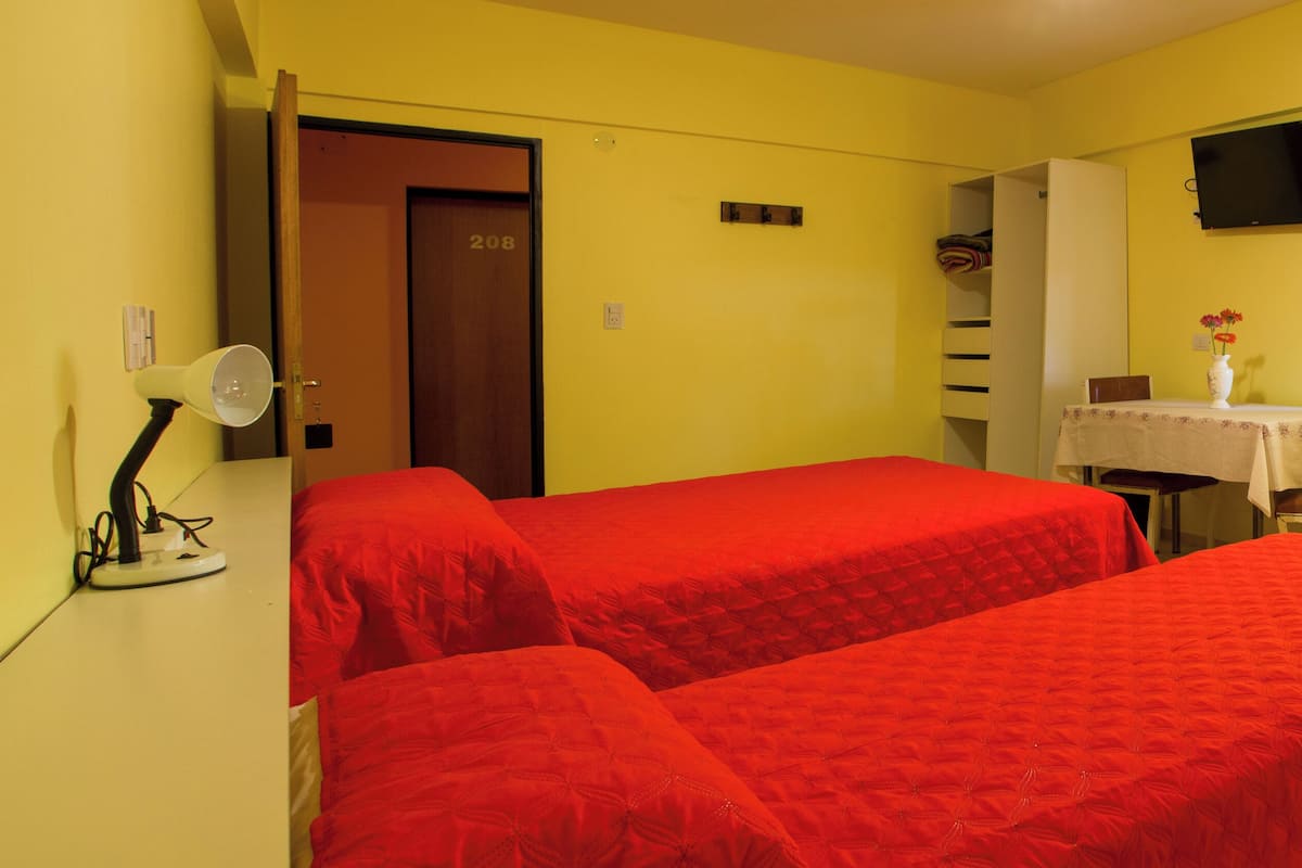 Una habitación con dos camas, un escritorio con una silla, un televisor en la pared y una puerta con el número 208.