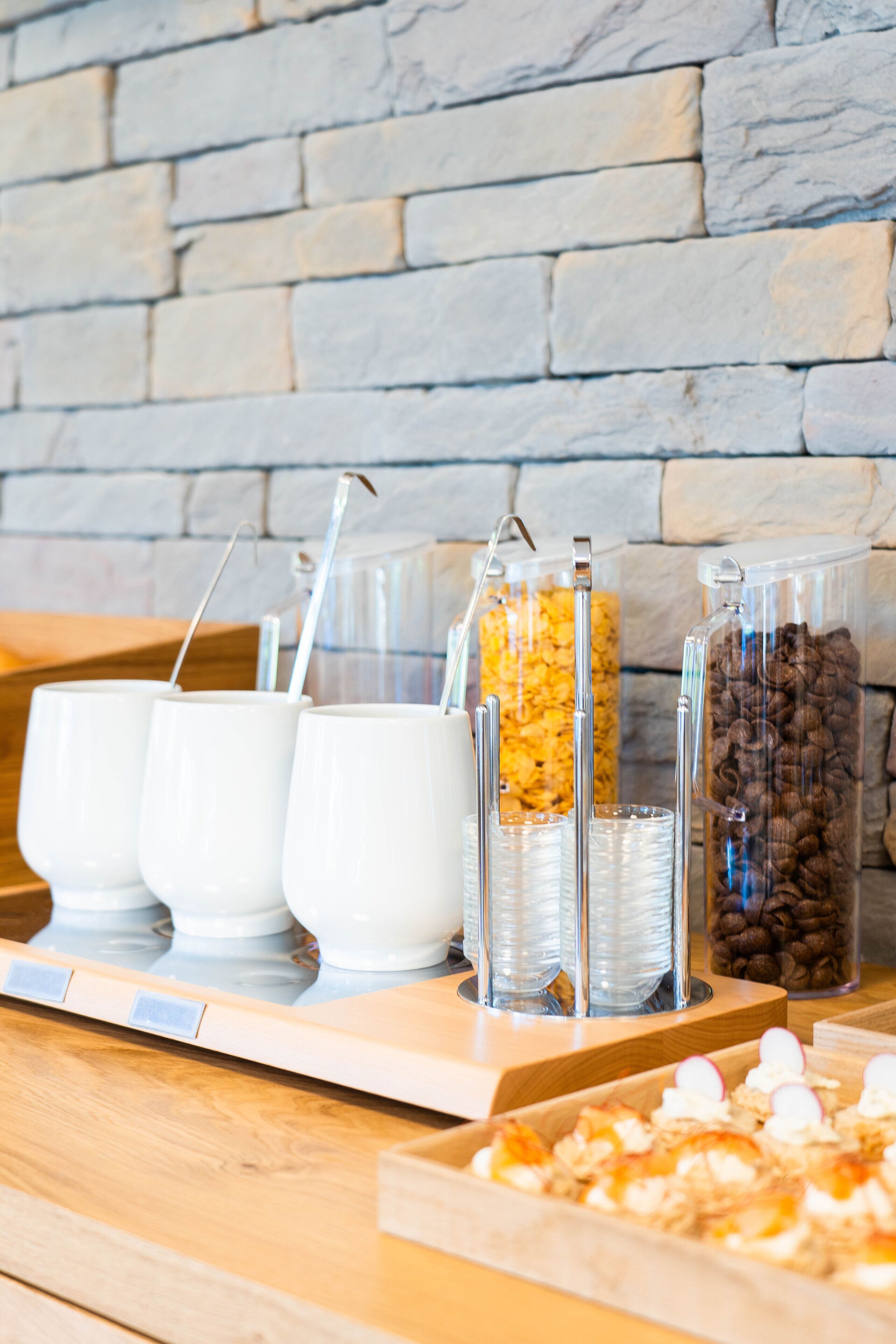 Ein Frühstücksbuffet mit weißen Tassen, Halmen und Behältern für Müsli und Kaffeebohnen.