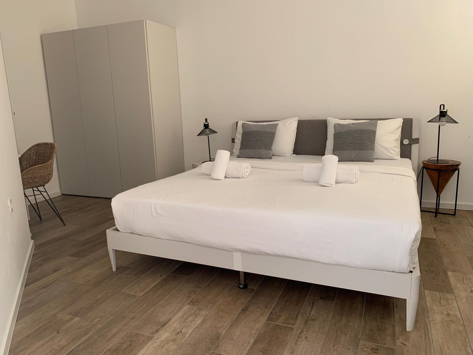 A neatly made bed with white linens, a grey headboard, and a bedside lamp.