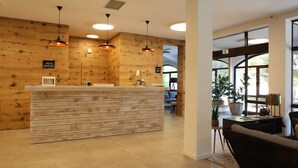 A reception area with a wooden reception desk, pendant lighting, and a view of the lounge area. - Hotel Ortus Residence (Ankaran)