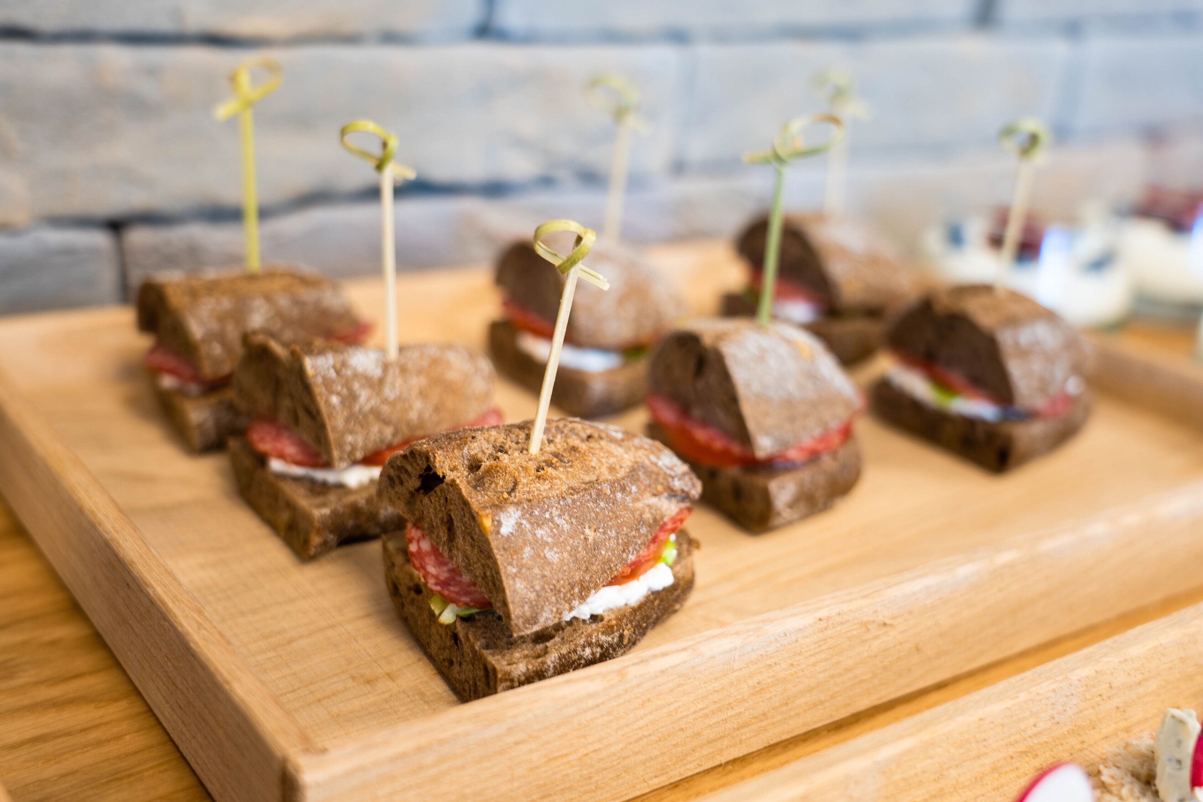 Una tabla de madera con varios sándwiches, cada uno sujeto con un palillo.