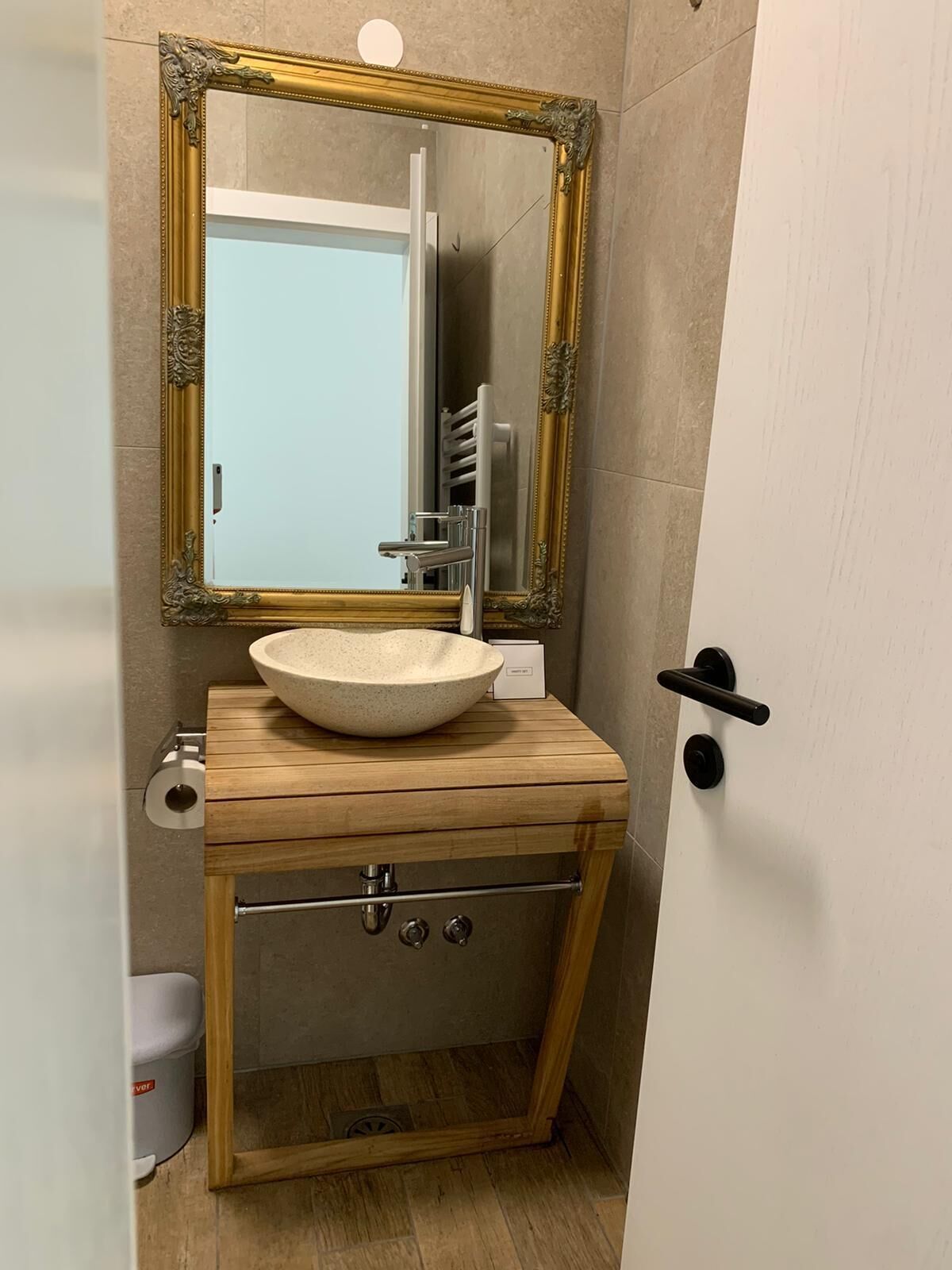 A bathroom with a wooden vanity, a large mirror with an ornate gold frame, a white sink, and a towel rack.