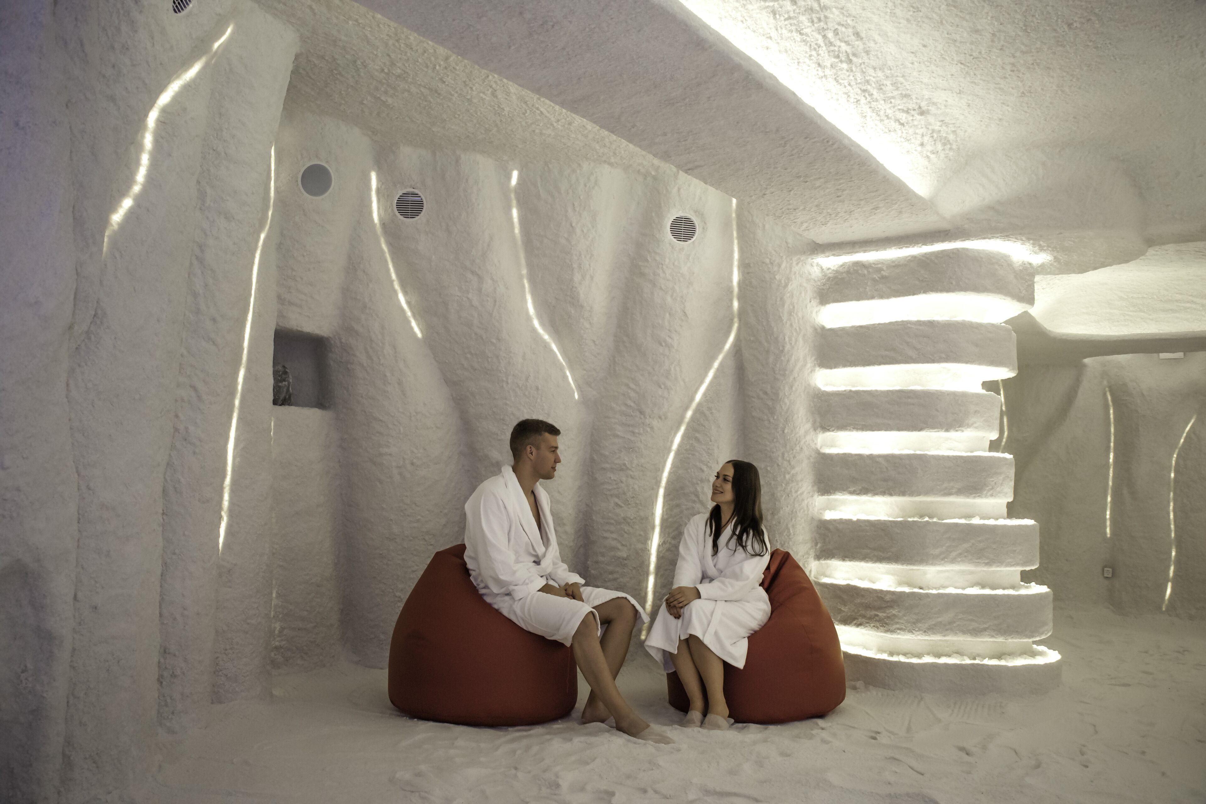 Um casal sentado em sacos de feijão em um quarto com um design de parede texturizado e uma luminária em formato de escada.