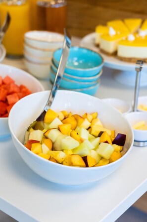 Un bufé de desayuno con diversas frutas y un vaso de zumo de naranja.