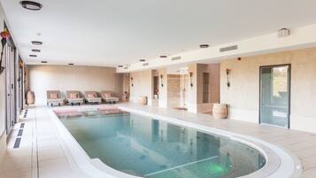 A large indoor swimming pool with lounge chairs and a spa area.