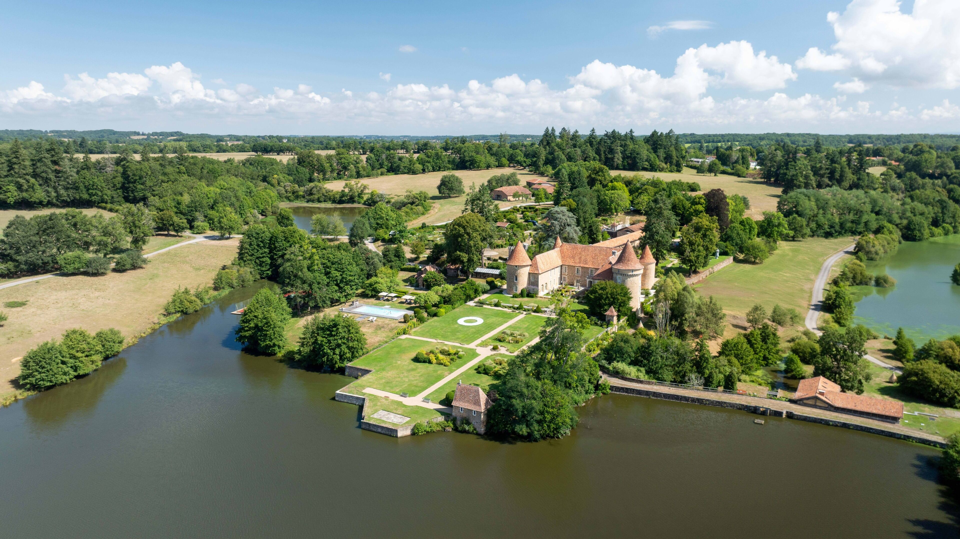 Ein Luftbild eines schlossartigen Anwesens mit Burggraben, umgeben von üppiger Vegetation und einem Fluss.