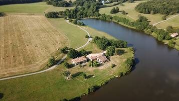 Luchtbeeld van een landgoed in het buitengebied met een groot veld, een rivier en een huis met een rood dak.