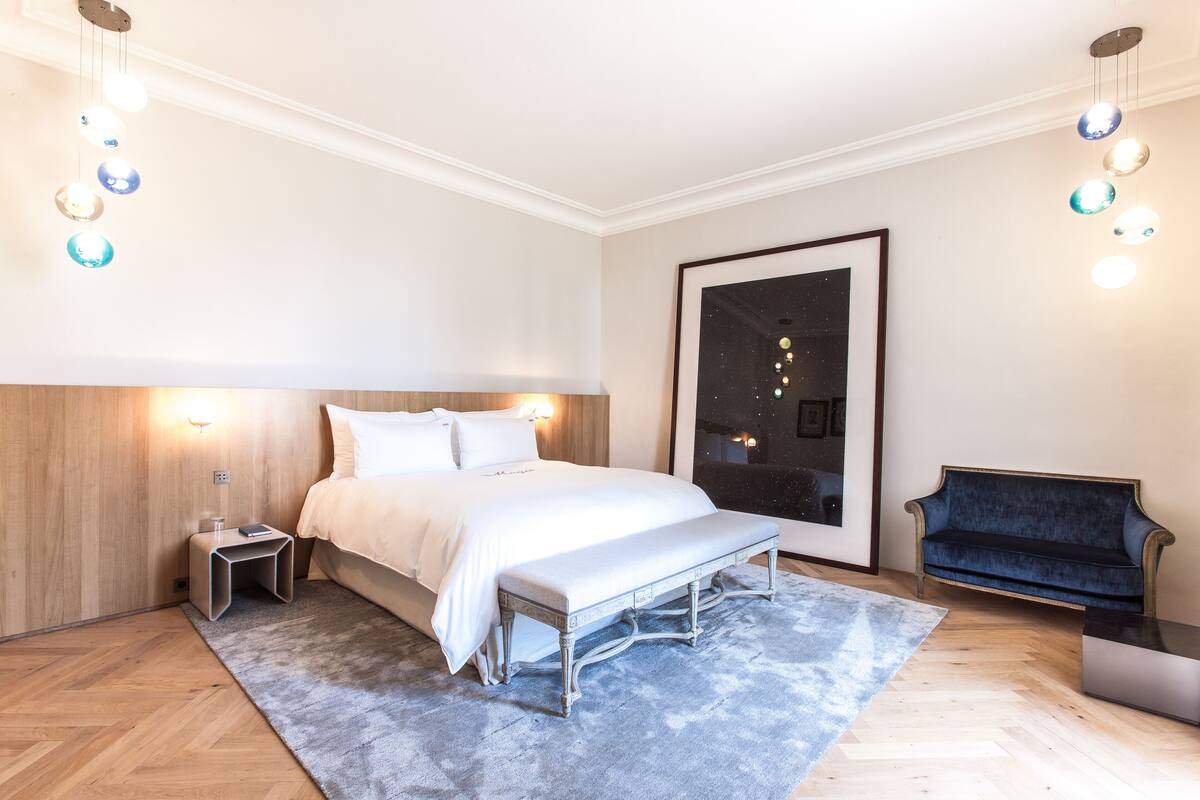 Une chambre à coucher moderne avec un grand lit, des tables de chevet, un banc, un canapé et un tableau encadré au mur.