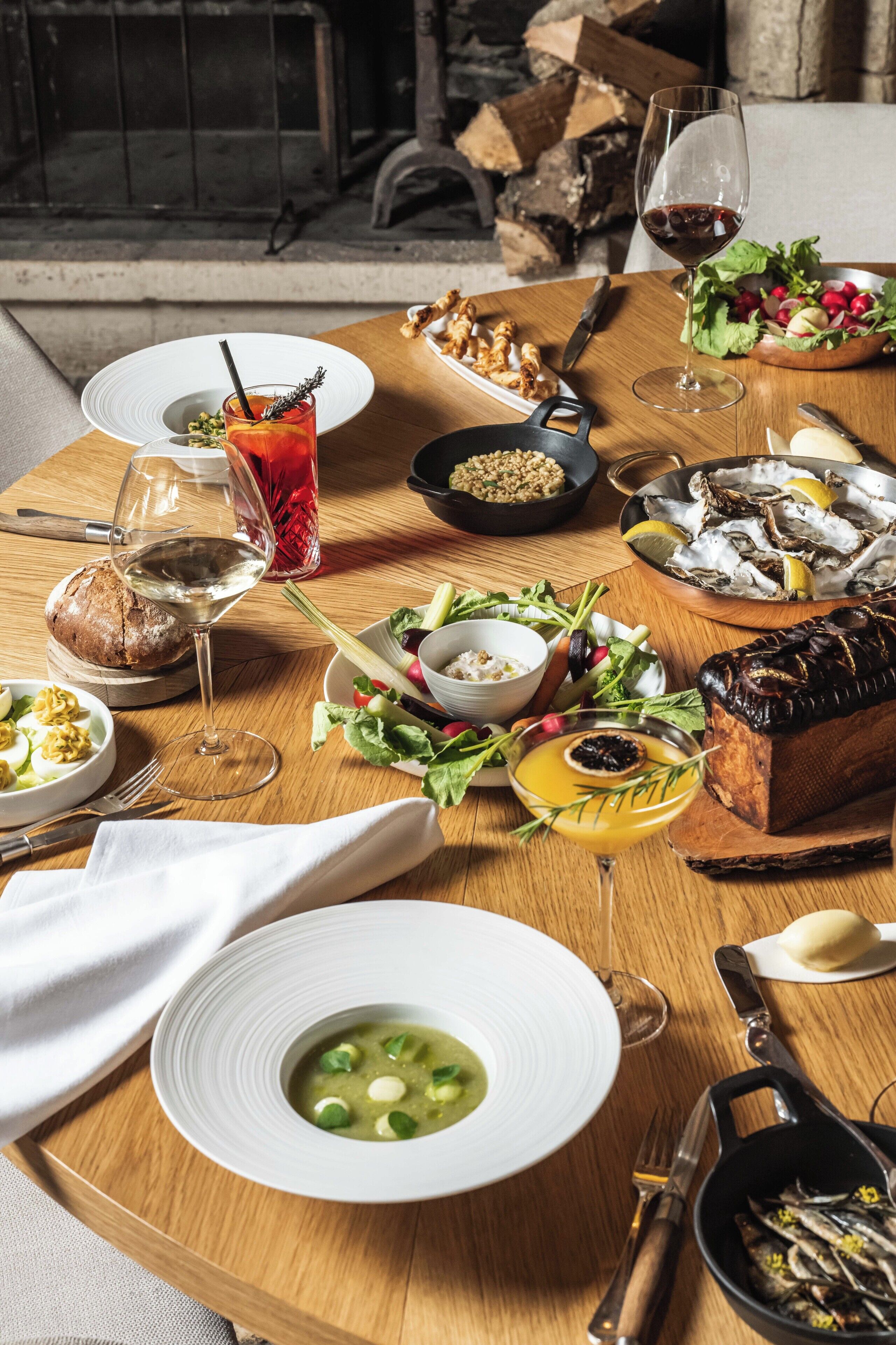 A wooden dining table with various dishes, including seafood, salad, and bread, along with wine glasses and a pitcher.
