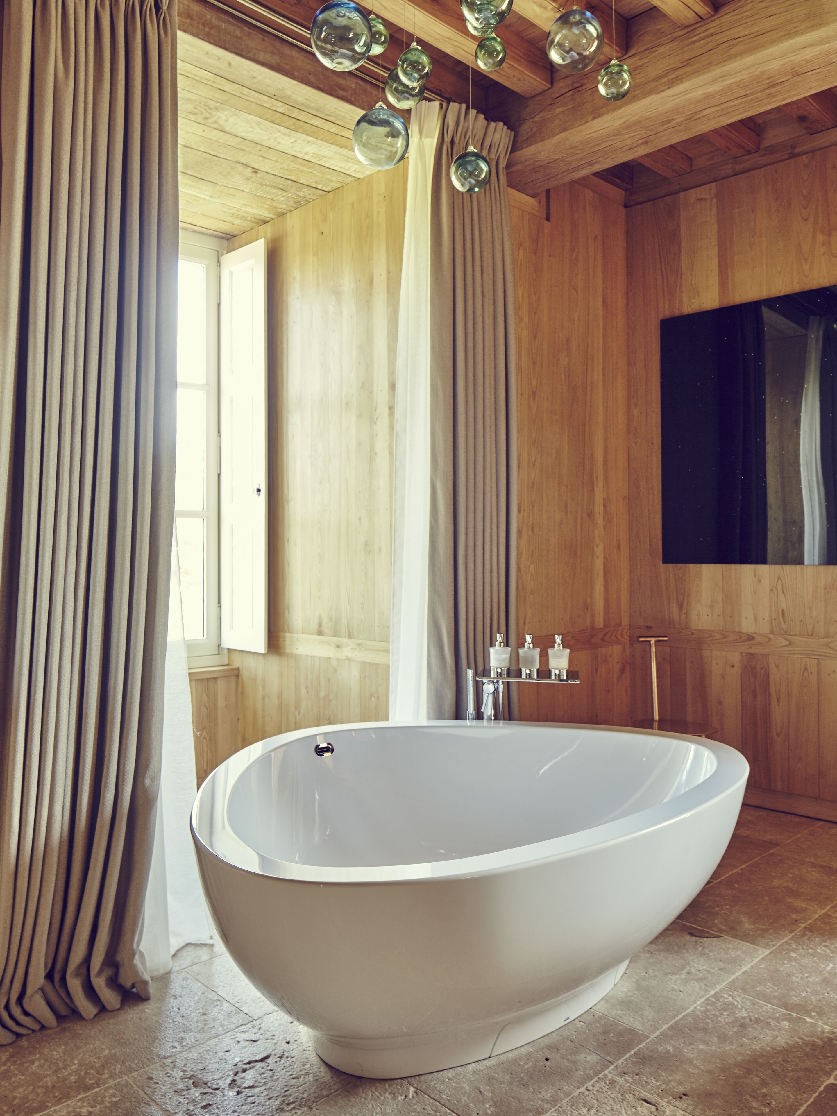 Une salle de bain moderne avec une baignoire sur pieds, un lambris en bois et une grande fenêtre agrémentée de rideaux.
