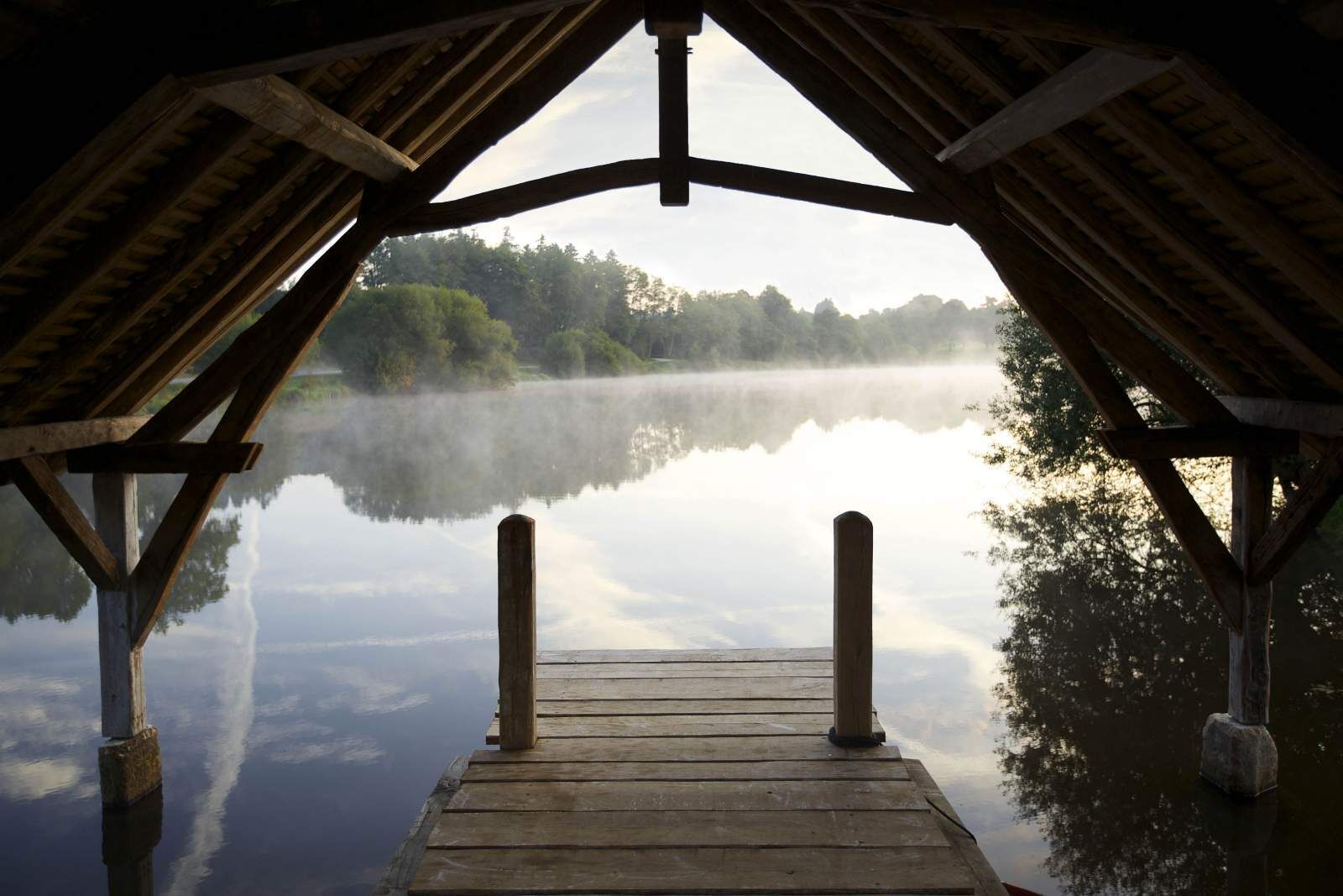 A wooden pier leading to a calm lake with a forested background.