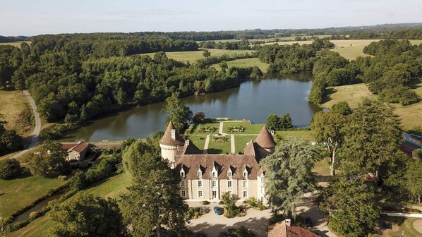 A large, historic building with a moat and a lake, surrounded by lush greenery and a well-maintained lawn. - Domaine des Etangs, Auberge Collection (Massignac)