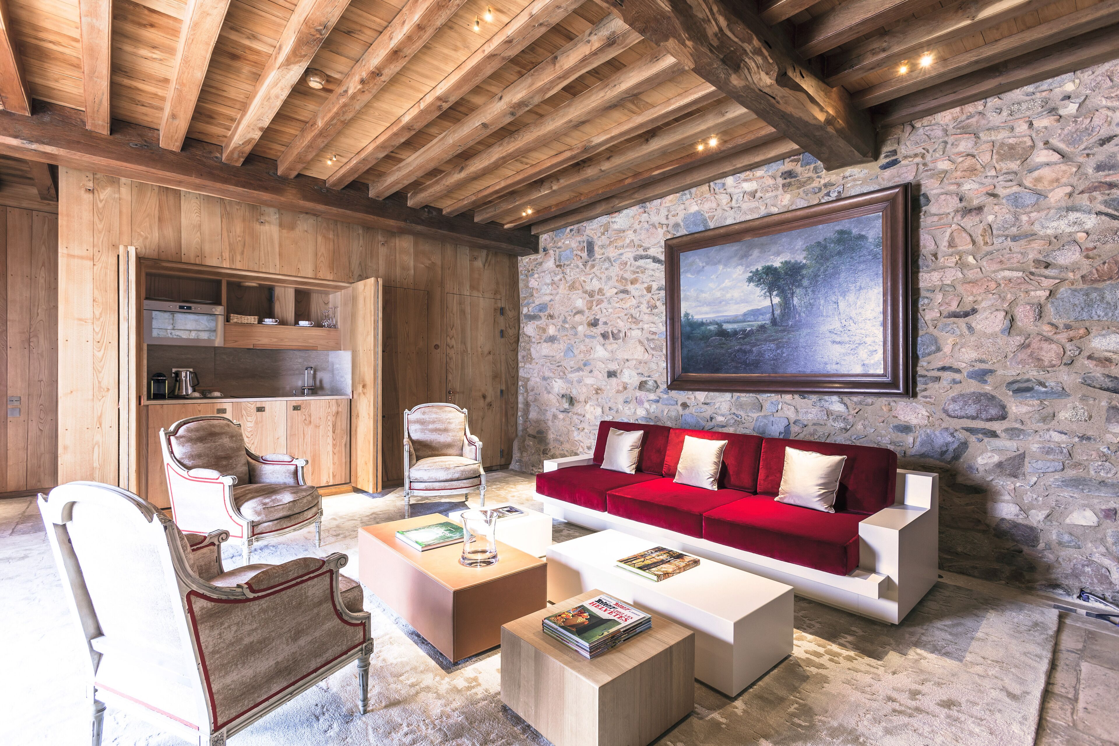 A cozy living room with wooden beams, a stone wall, a red sofa, and a painting.