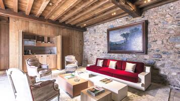 A cozy living room with wooden beams, a stone wall, a red sofa, and a painting.
