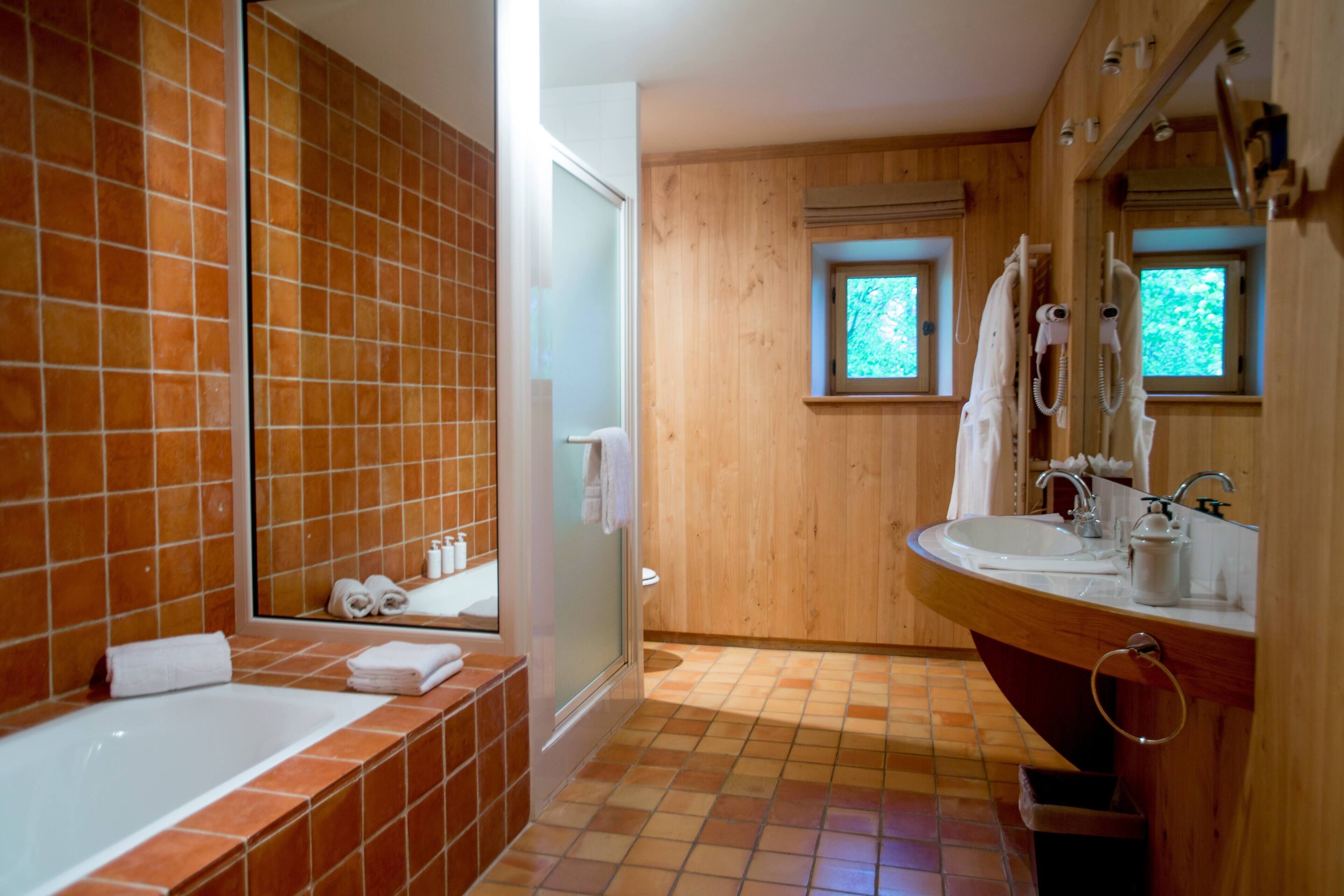 A bathroom with a wooden interior, a bathtub, a sink, and two windows.