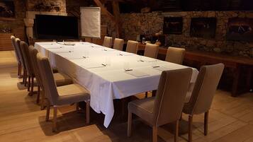 A long dining table with chairs, a white tablecloth, and a stone wall in the background.