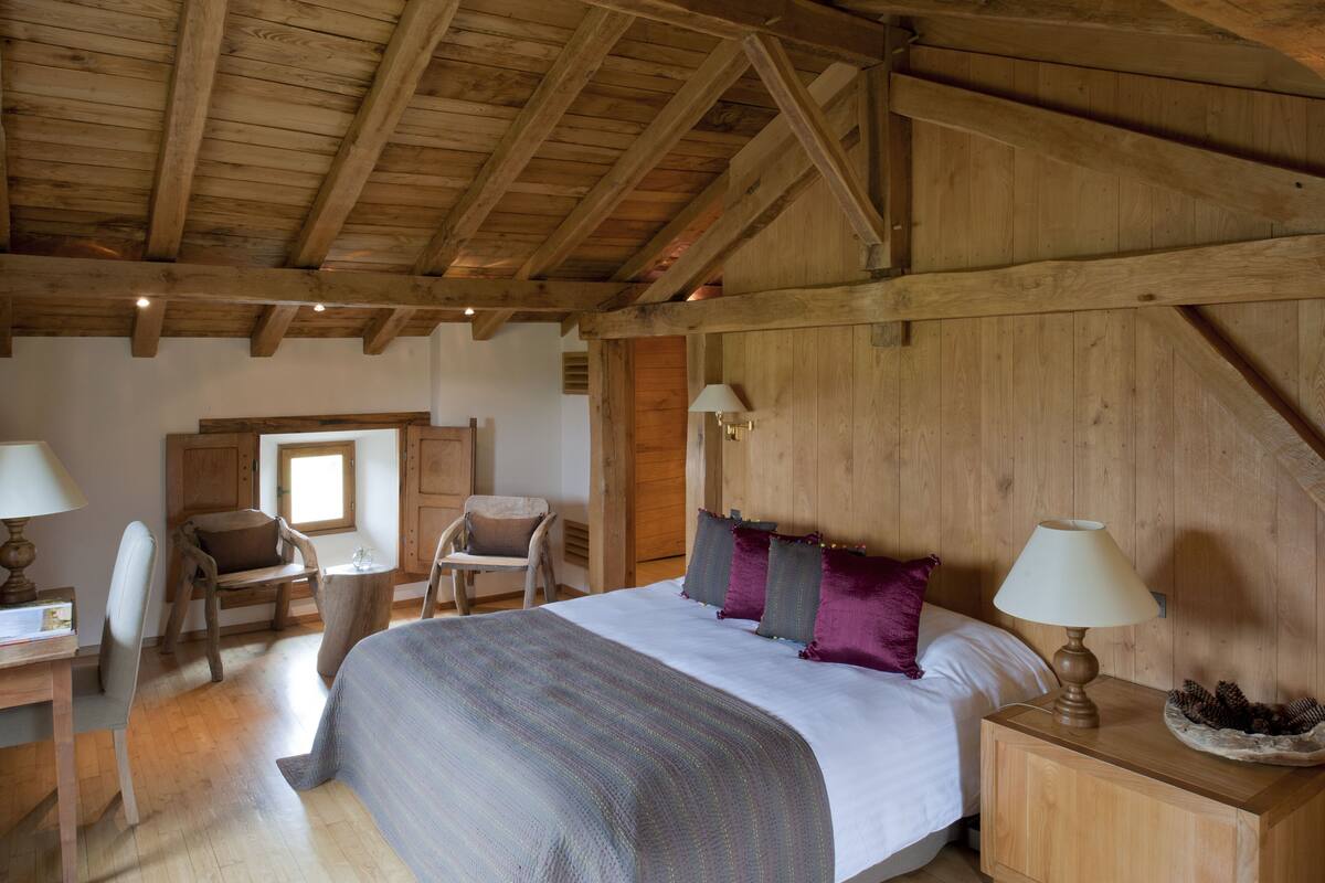 Une chambre à coucher rustique en bois, avec un grand lit, deux chaises, un bureau et une lampe.