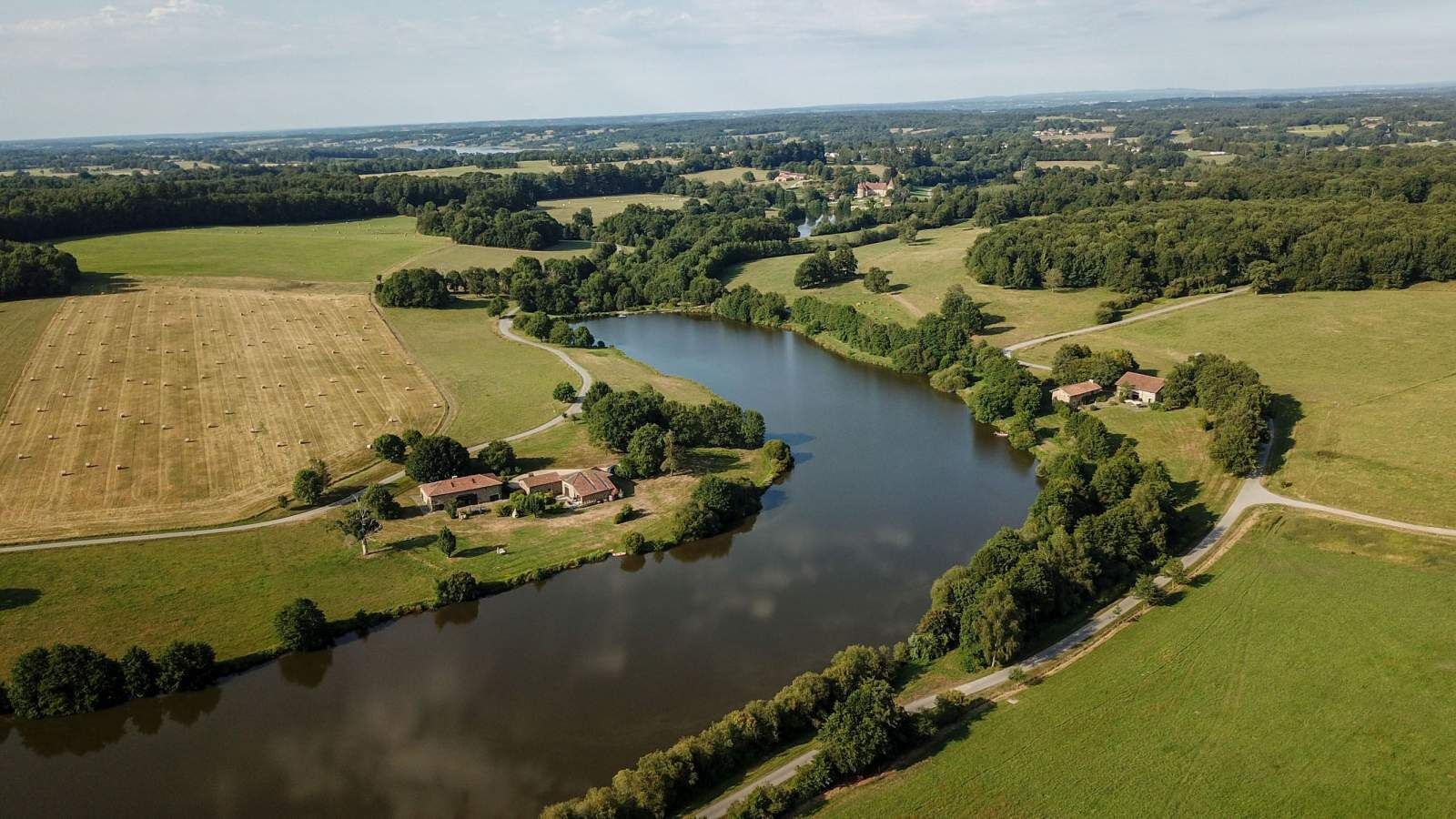 Eine Luftaufnahme einer ländlichen Landschaft mit einem Fluss, Feldern und einigen Gebäuden.