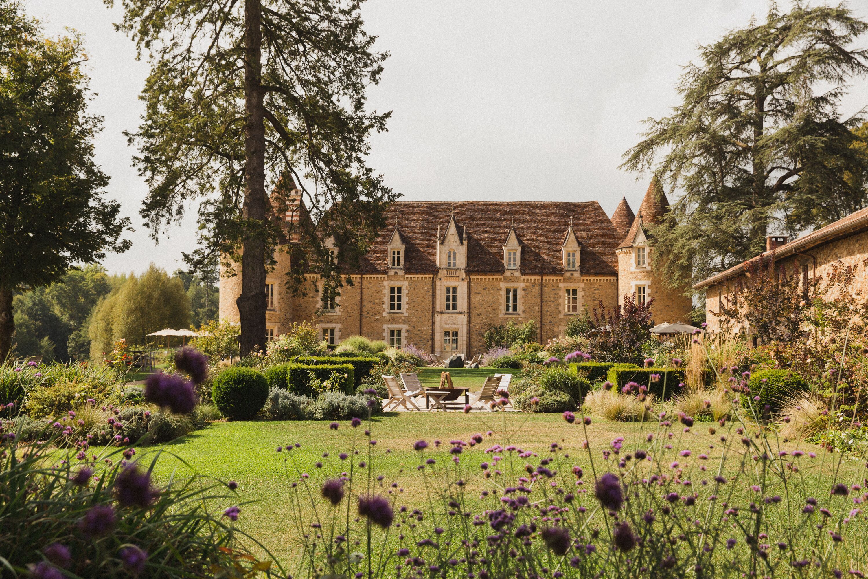 A large, historic building with a symmetrical facade, a well-manicured garden with a lawn and flower beds, and a clear sky.
