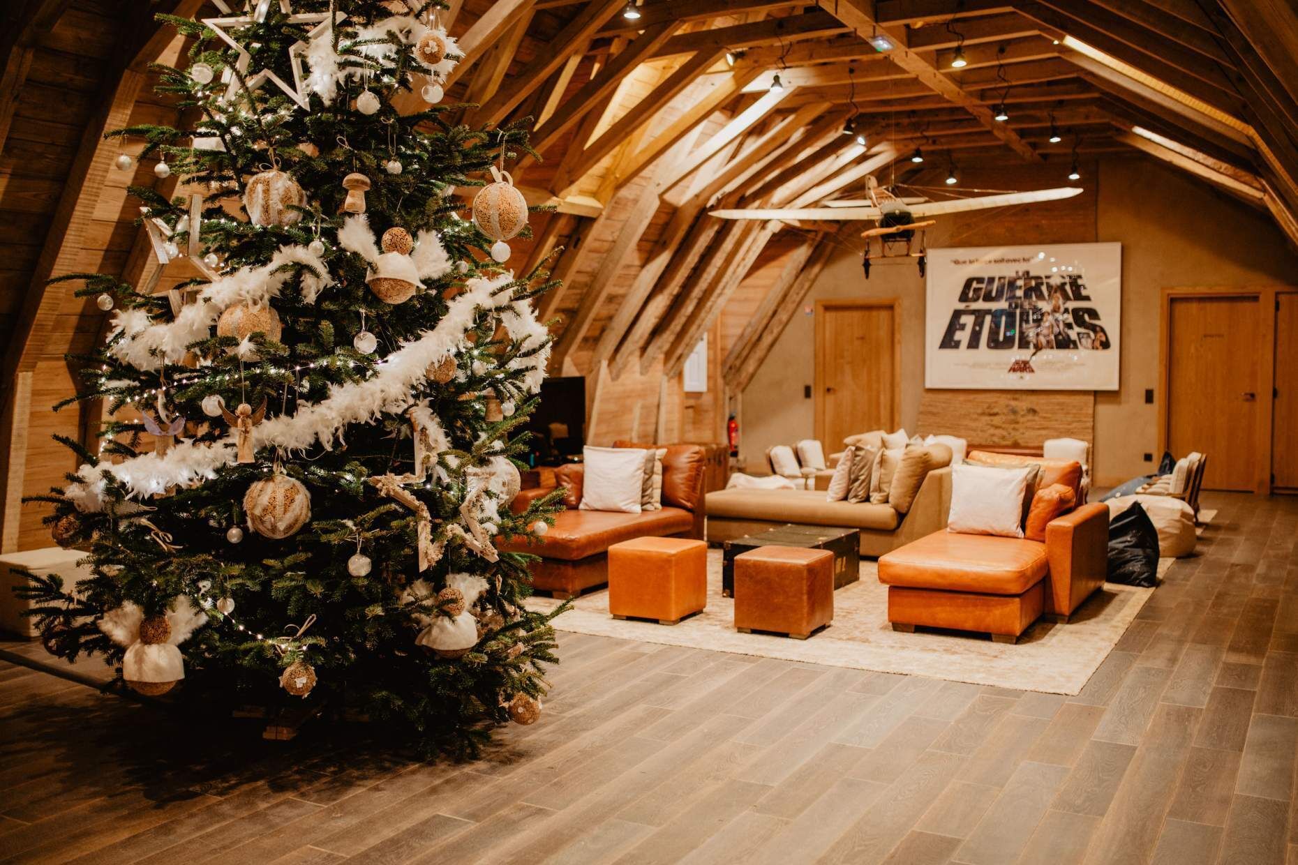 Une pièce chaleureuse de style loft, avec un grand sapin de Noël, des canapés en cuir et un plafond en bois.