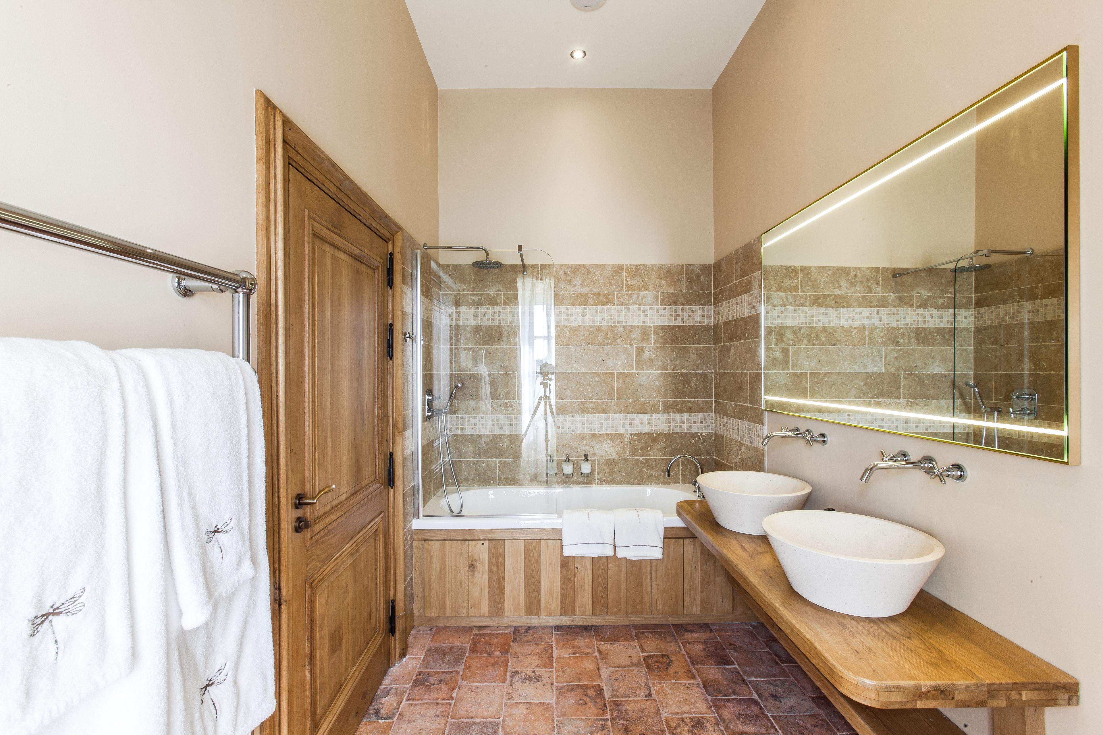 A bathroom with a wooden vanity, two sinks, a bathtub, and a glass shower enclosure.