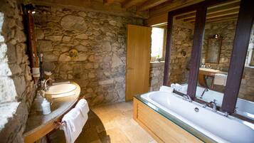 A stone-walled bathroom with a wooden vanity, a large bathtub, and a mirror with a wooden frame.