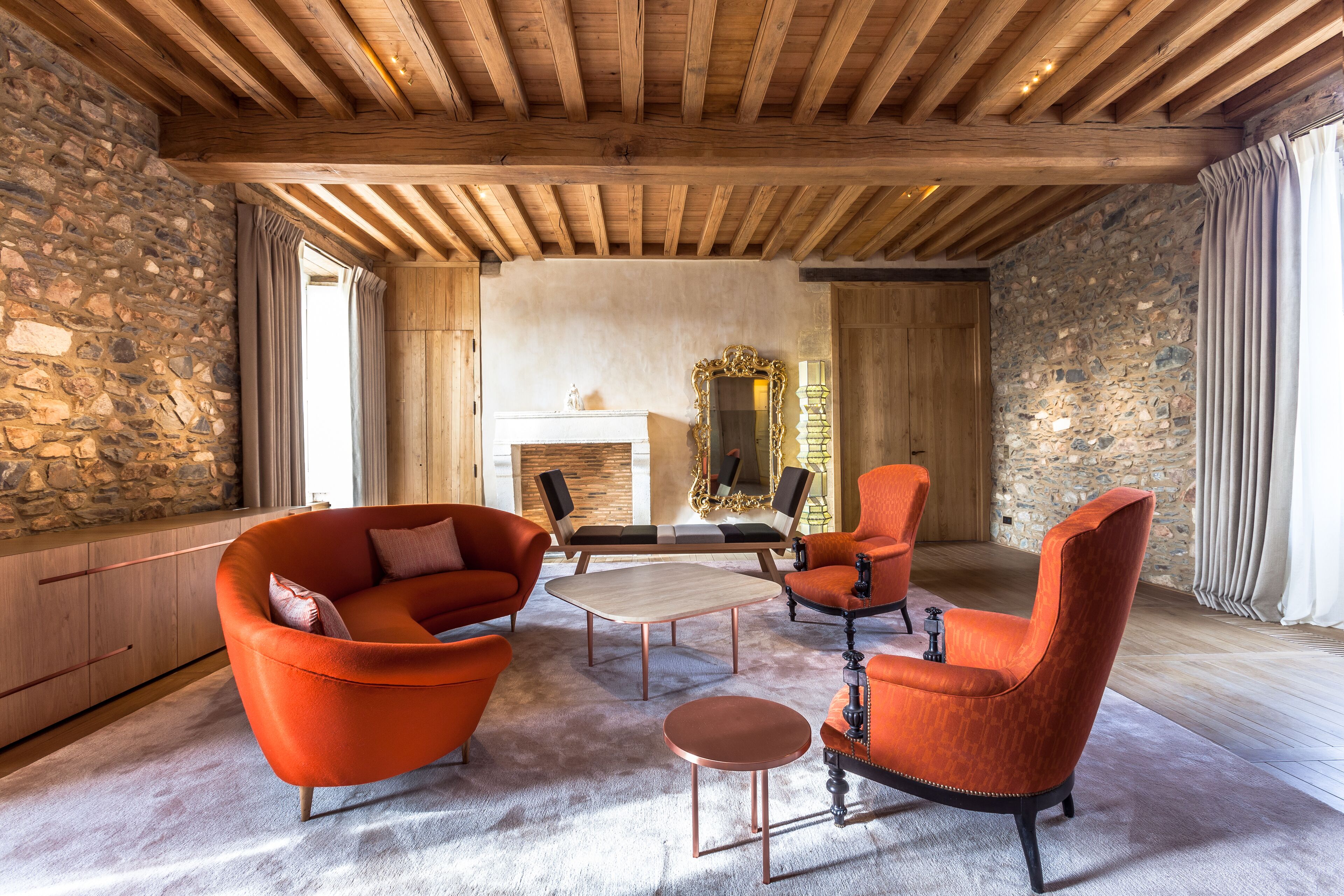 A spacious living room with a stone wall, wooden ceiling beams, and a fireplace.