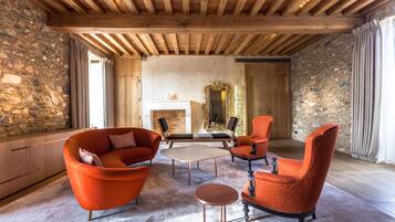 A spacious living room with a stone wall, wooden ceiling beams, and a fireplace.