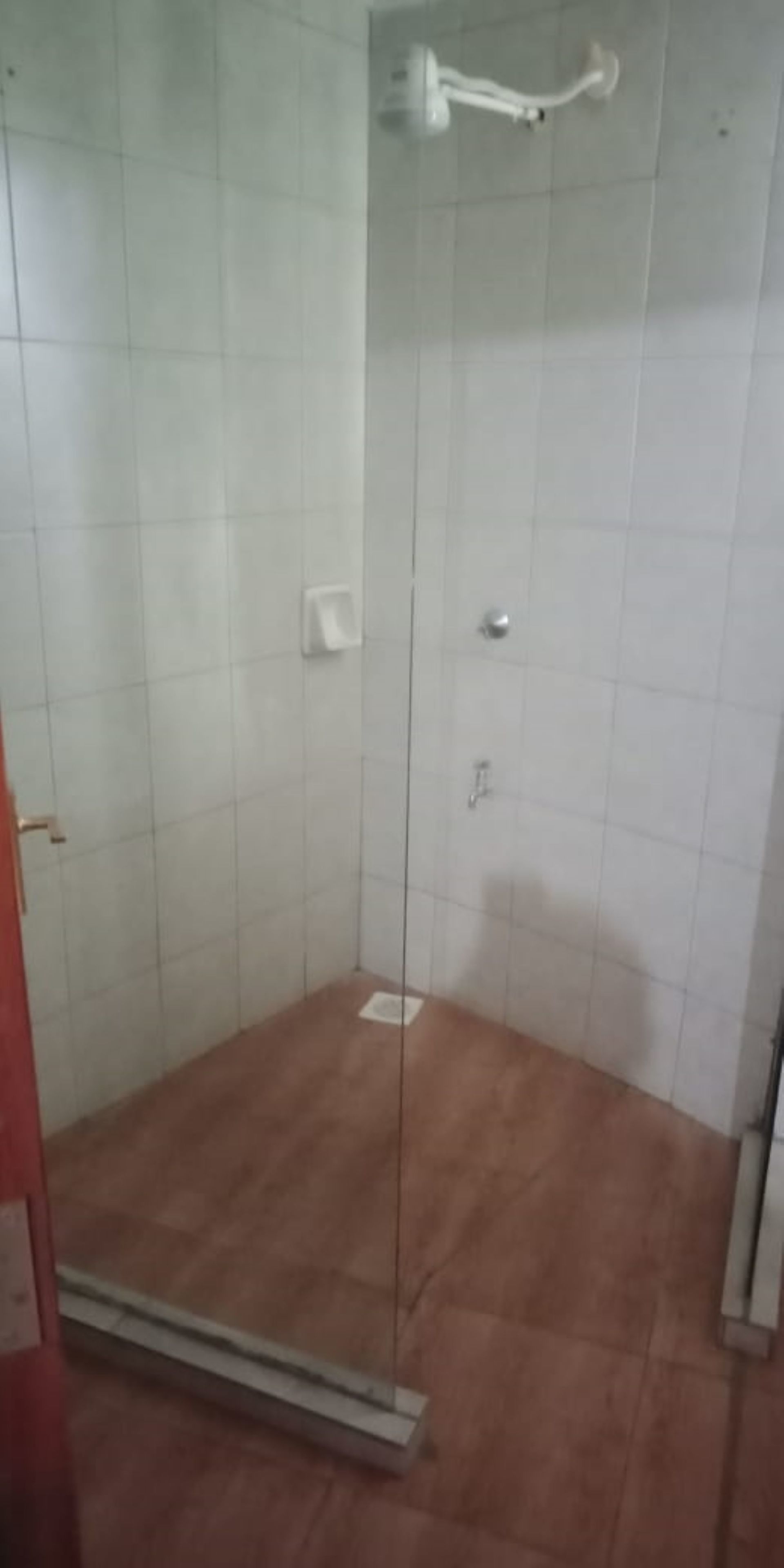 A shower area with white tiled walls, a glass door, and a brown floor.