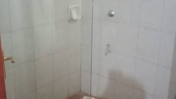 A shower area with white tiled walls, a glass door, and a brown floor.