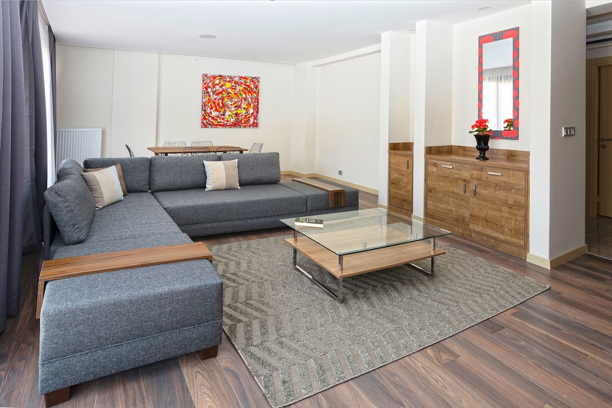A modern living room with a sectional sofa, a glass coffee table, and a dining area with a table and chairs.