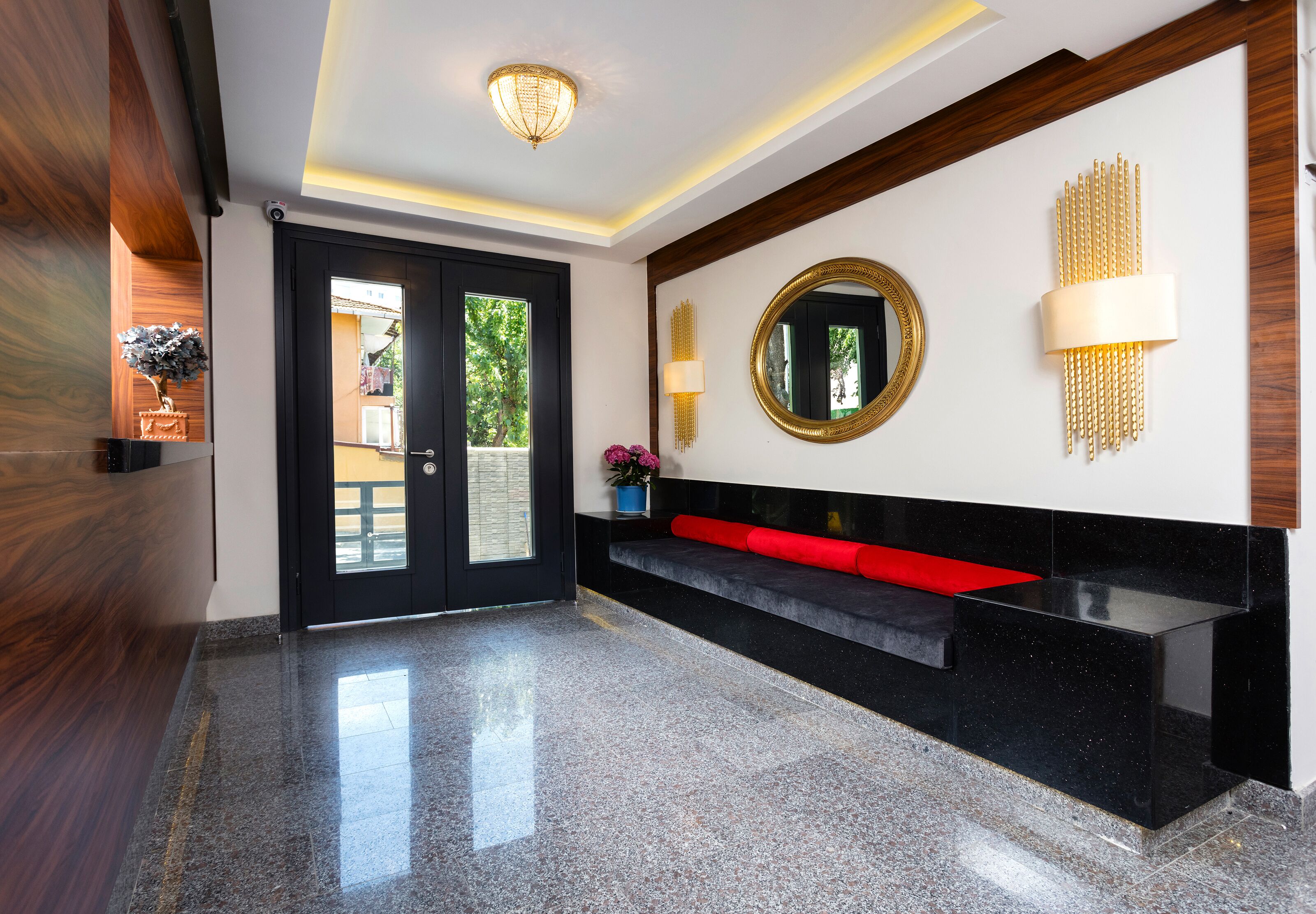 Un vestíbulo moderno con un mostrador de recepción negro, un banco rojo, un espejo redondo y una lámpara fijada a la pared.